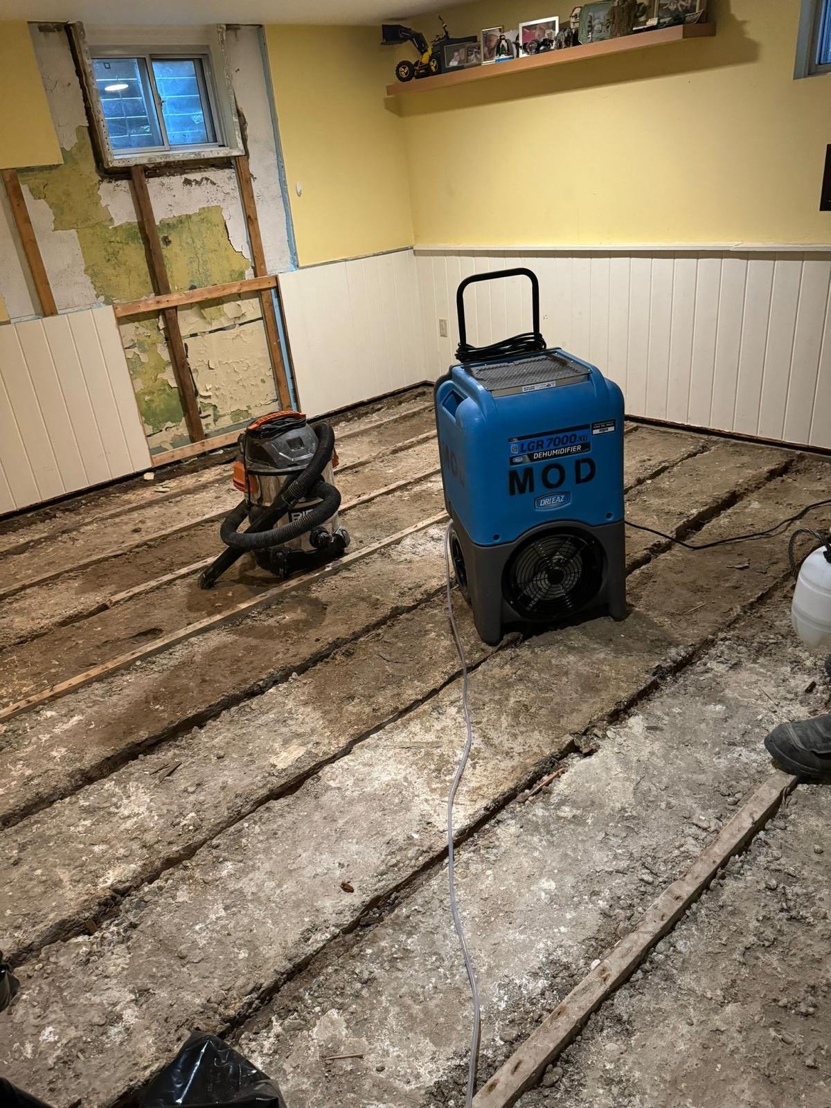 Basement under drying after water damage with dehumidifier and subfloor exposed